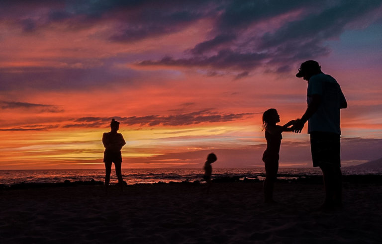 A family backlit to a gorgeous Hawaiian sunset on the beach.