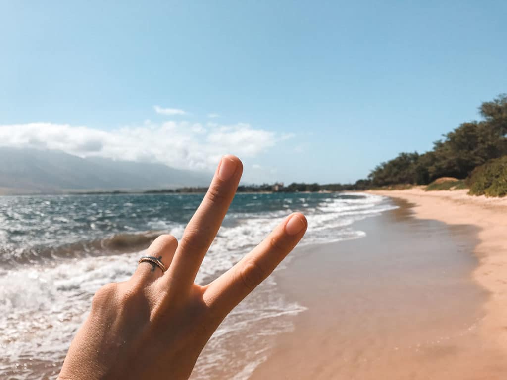 A hand making a peace sign at a beach in Hawaii. 