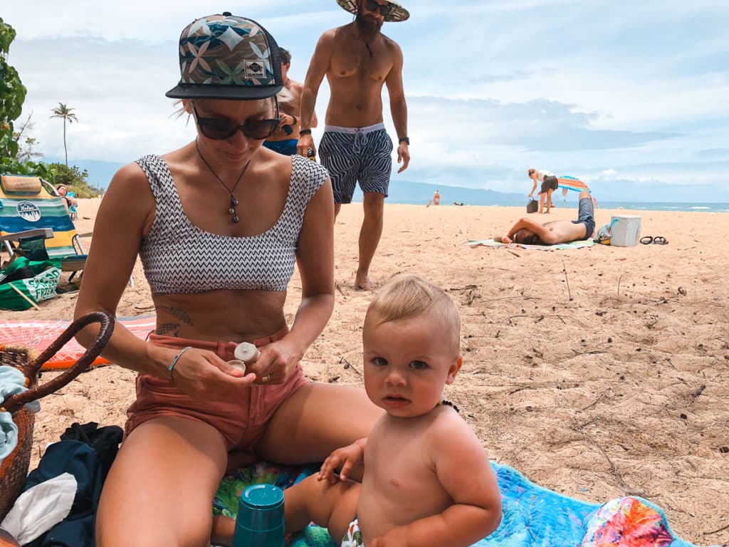 A mom applying sunscreen to a baby on the beach in Hawaii.