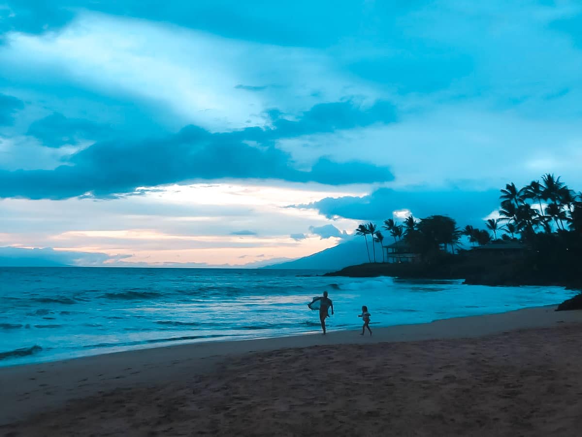 A mom playing with her kids on the beach in Hawaii and a beautiful sunset in the background.