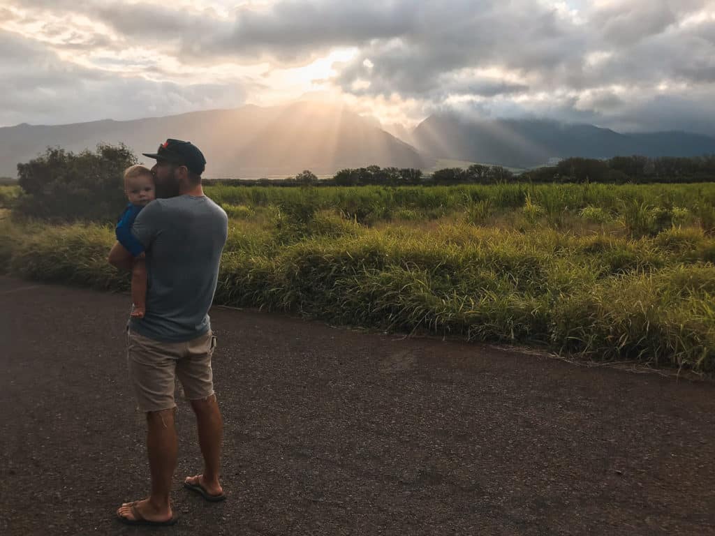 Dad holding a baby and kissing his head in front of the West Maui Mountains in Maui, Hawaii.