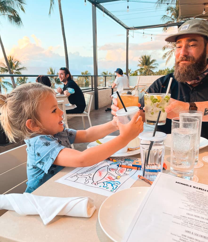 A toddler cheersing dad at family-friendly restaurant on Maui. 