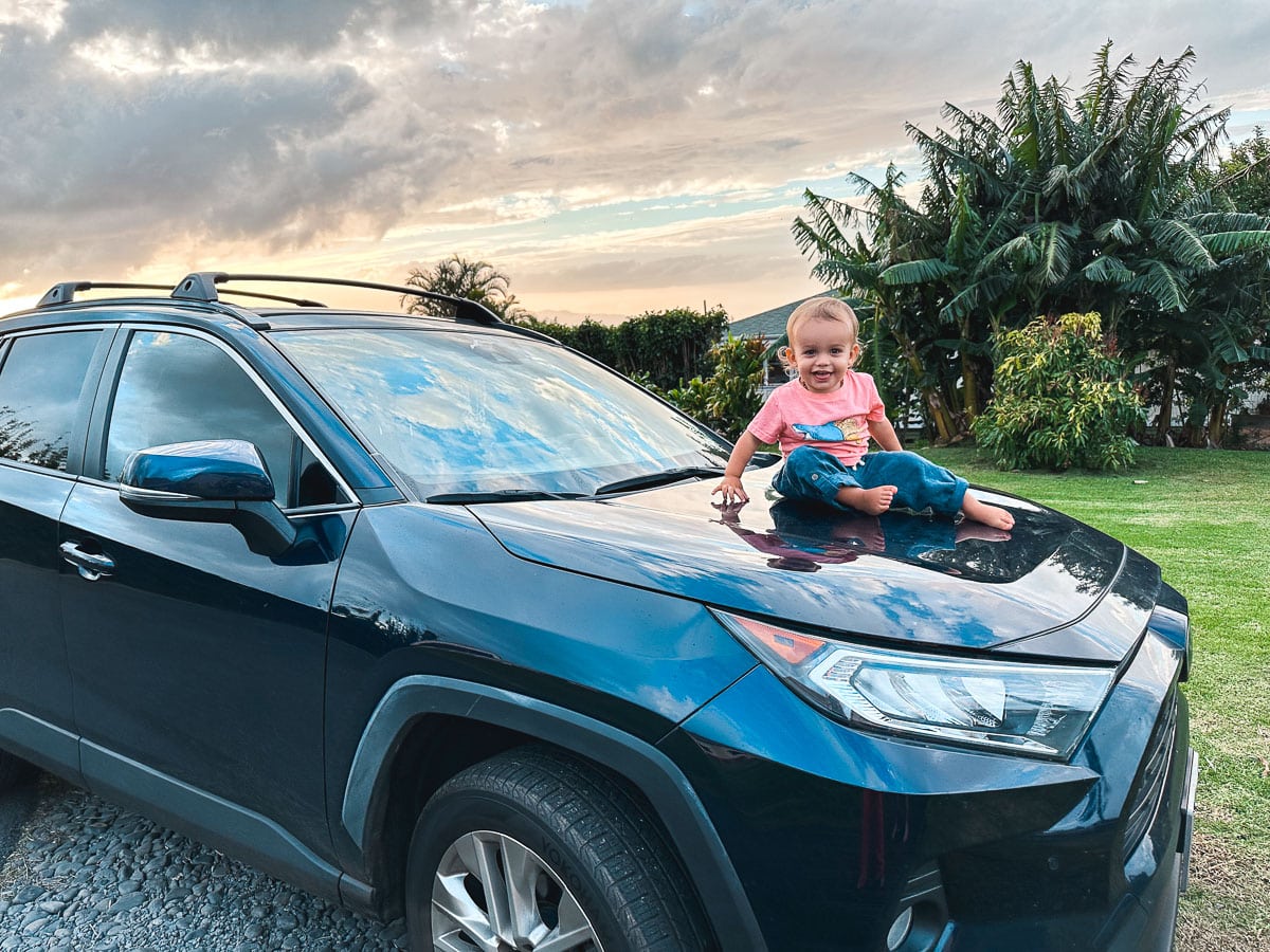 Baby sitting on top of a car in Maui, Hawaii with a beautiful sunset in the background.