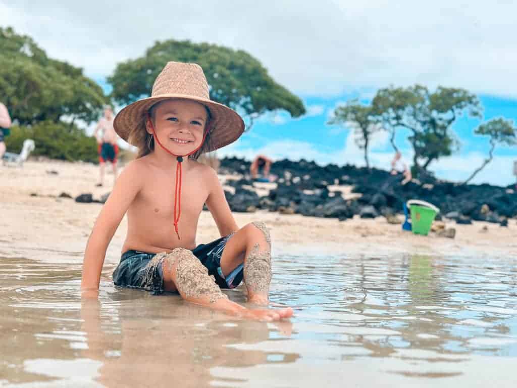 A boy wearing sun hat while playing in the ocean on the Big Island of Hawaii 