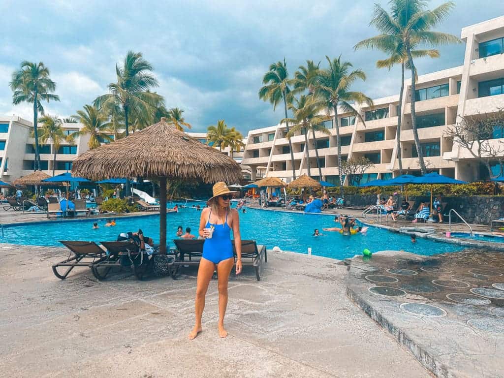 Woman Standing in front of pool with a drink in hand at Outrigger Kona Resort and Spa. 