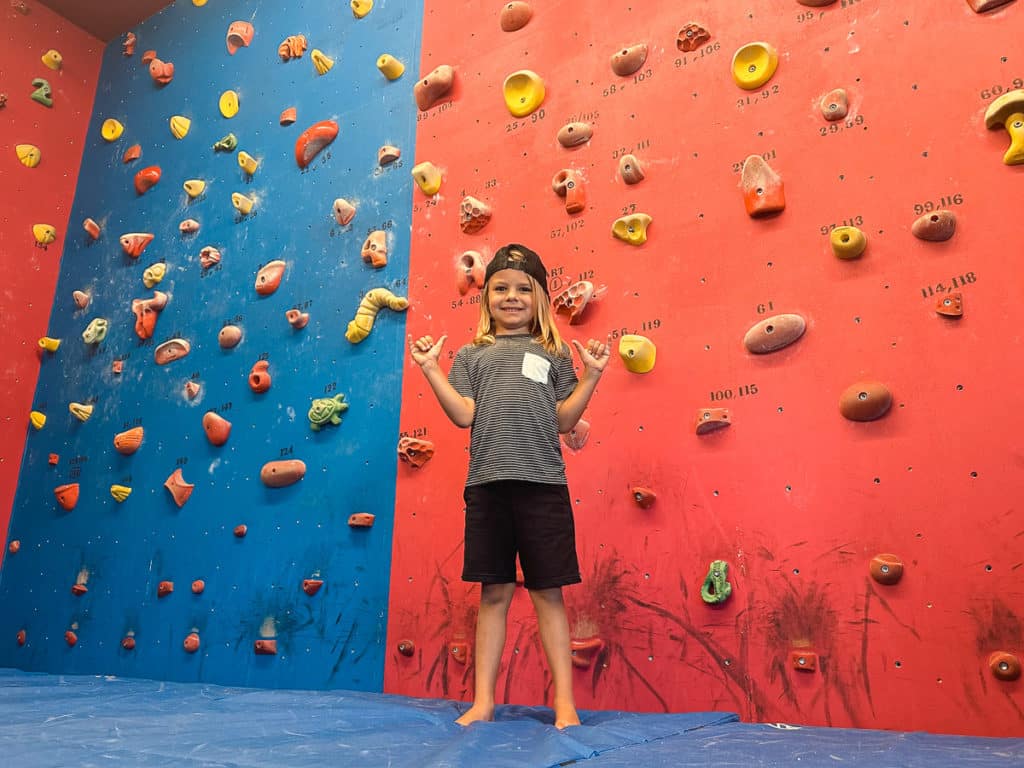 A kid standing in front of a climbing wall at Big Island Climbing Gym in HIlo, Hawaii. 