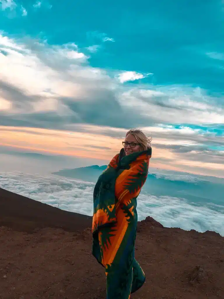 A woman standing on the Haleakala Summit bundled up in a blanket. 