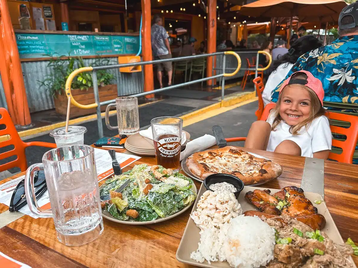 A smiling boy sitting in front of a table of pizza, chicken, an salad at Kona Brewing Company on the Big Island of Hawaii.