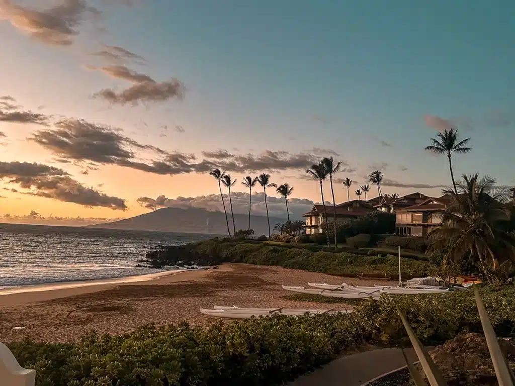 A Wailea Beach sunset with palm trees in the distance and outrigger canoes on shore