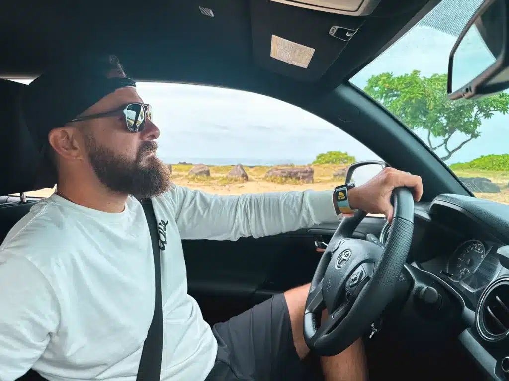 A man with his hand on the steering wheel, concentrating on the road while driving around the Big Island of Hawaii. 