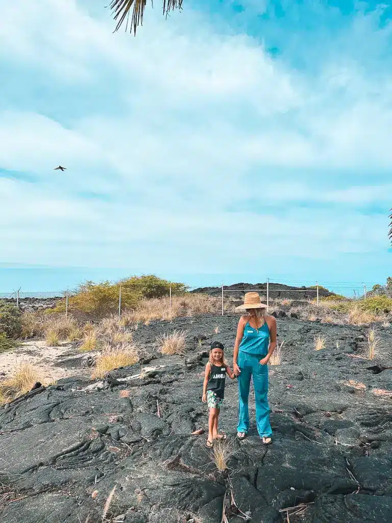 A mom and son holding hands and smiling while standing on lava rock in the Big Island of Hawaii. 