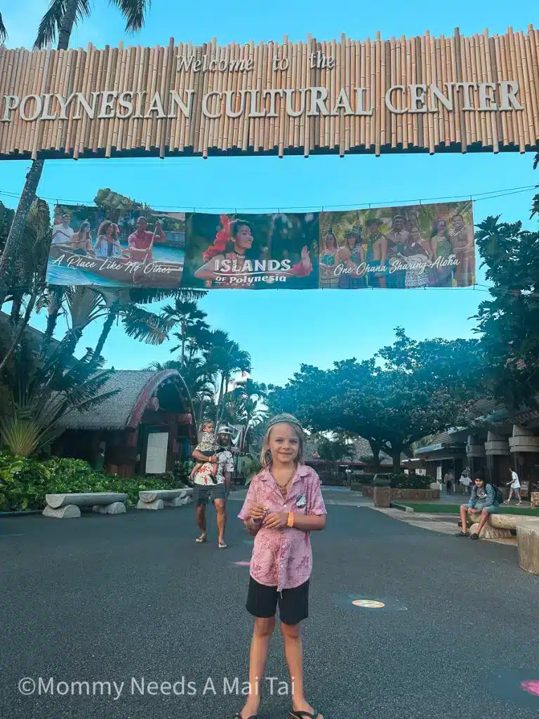 A boy smiling and standing under a sign that reads "Polynesian Cultural Center."