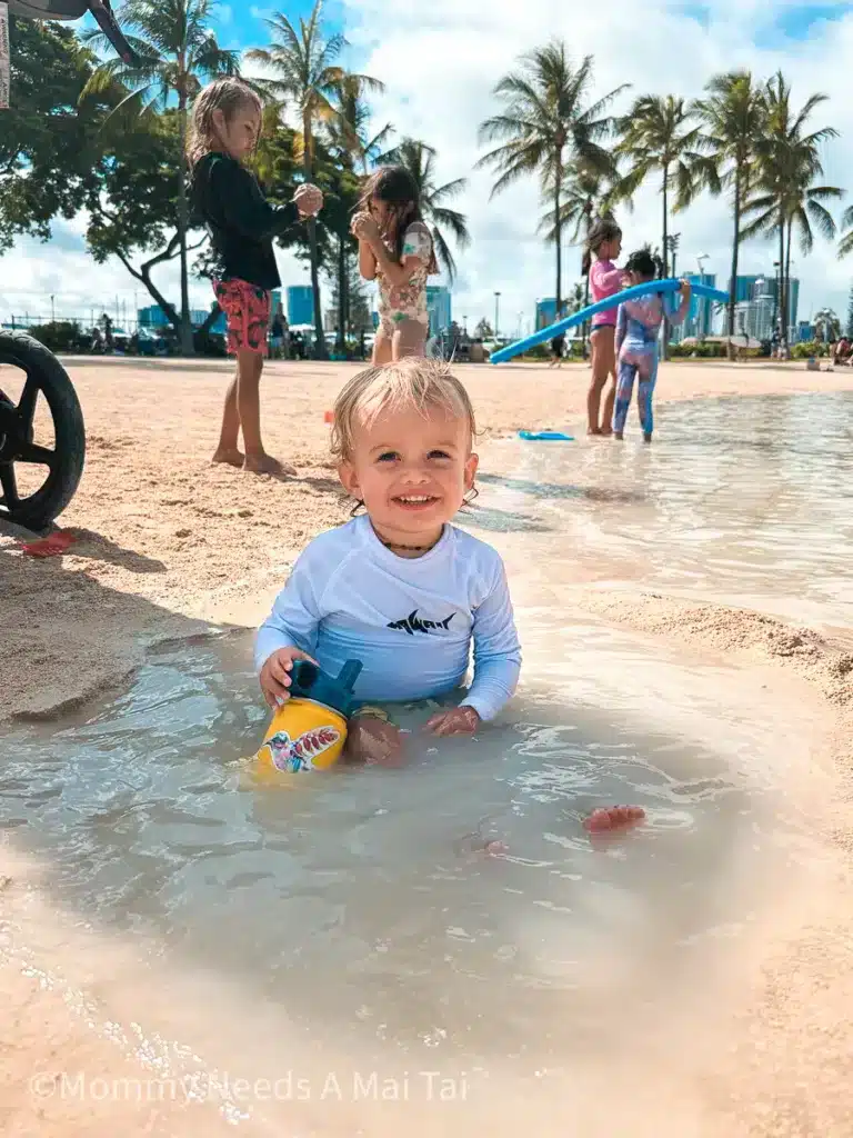 A baby smiling and playing while sitting in a tide pool at the Hilton Hawaiian Village in Waikiki, Oahu, Hawaii. 