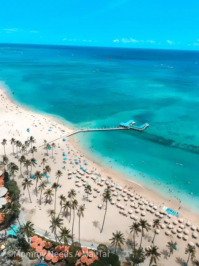 An arial view of Waikiki Beach with bright blue water meeting a sunny, blue sky on Oahu, Hawaii. 