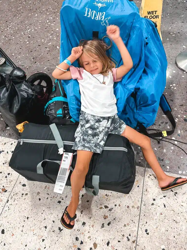 A young boy lays on top of a pile of luggage, looking tired at HNL Honululu, Oahu Airport. 