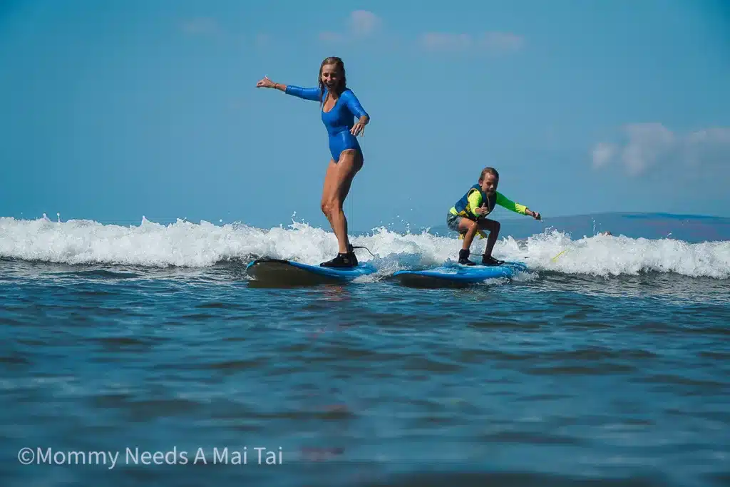 A mom and son looking excited and nervous as they stand up on surboards for the first time in Hawaii.