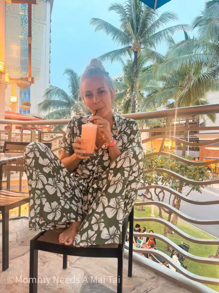 A woman in green floral aloha-wear sipping from a drink in Waikiki.