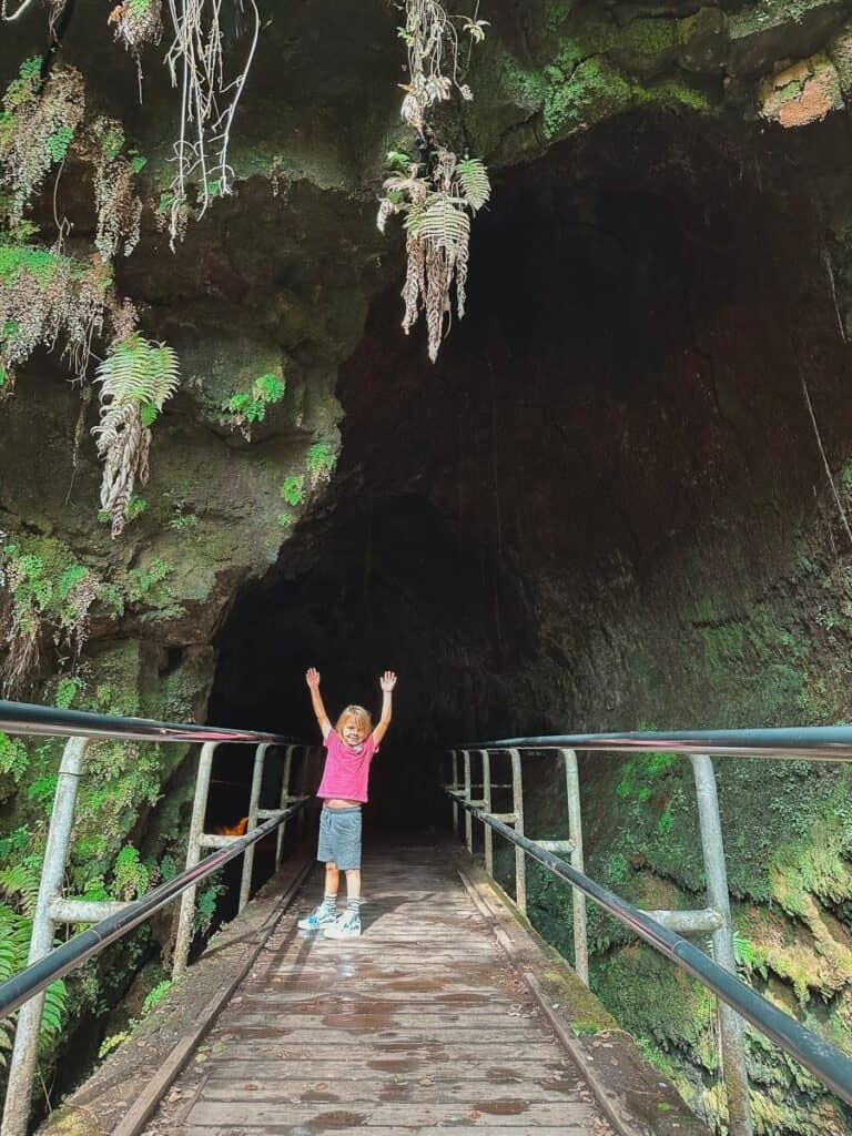 A kid standing with his hands up in the air at the entrance to the Thurston Lava tube on the Big Island of Hawaii