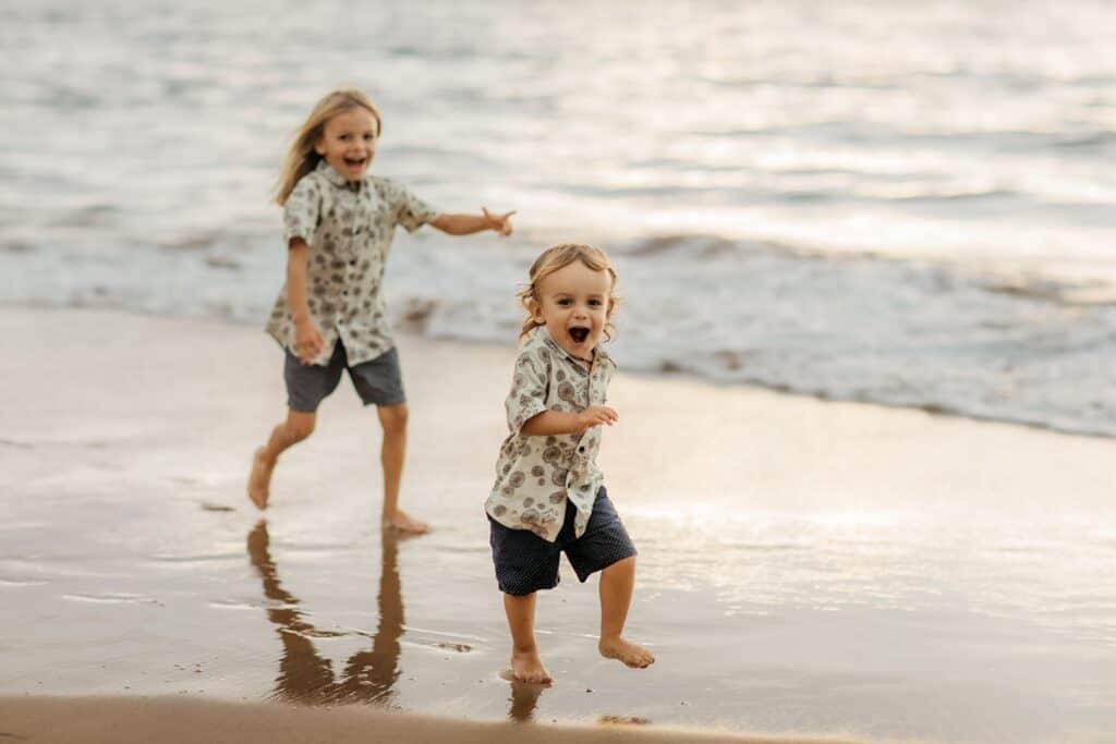 Two brothers in matching shirts chasing each other on a beach in Maui, Hawaii.