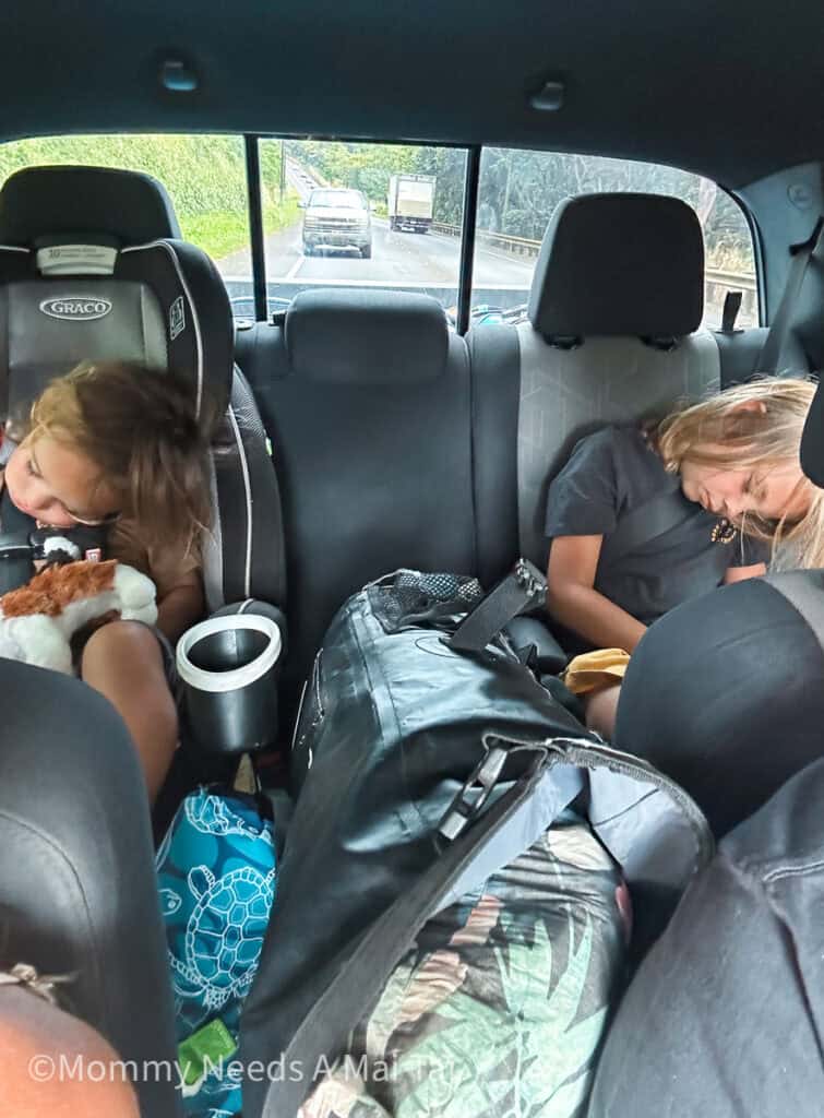 Two sleeping kids, strapped in car seats in the back of a car with their heads falling to one side. 