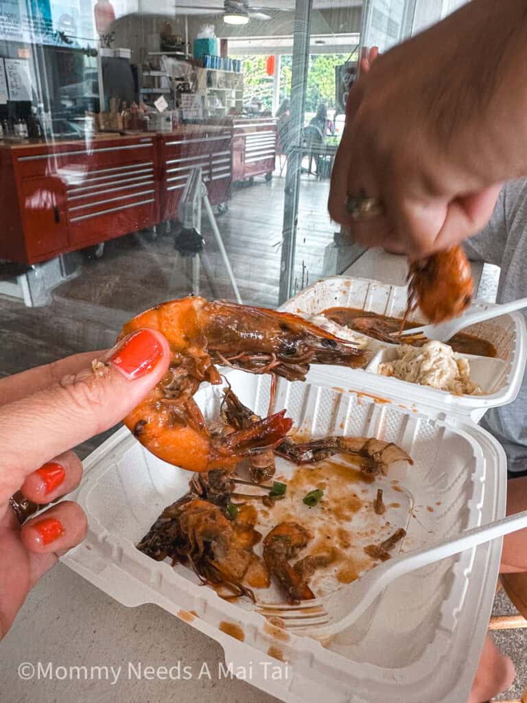 A hand holding up a garlic shrimp from Waking Up Delicious on Kauai.