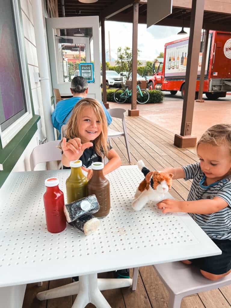 Two boys sitting at a table outside of Kauai Juice Co, giving shakas in Hawaii.