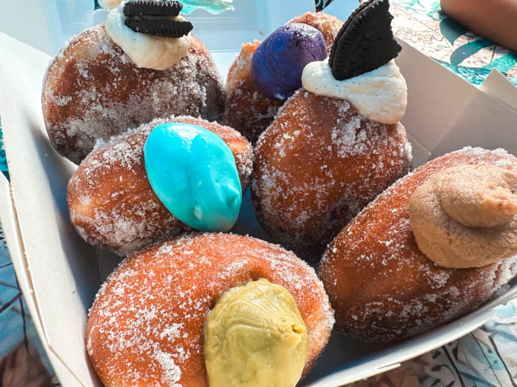 Six colorful malasadas lined up in a to go box from Passion Bakery on Kauai. 