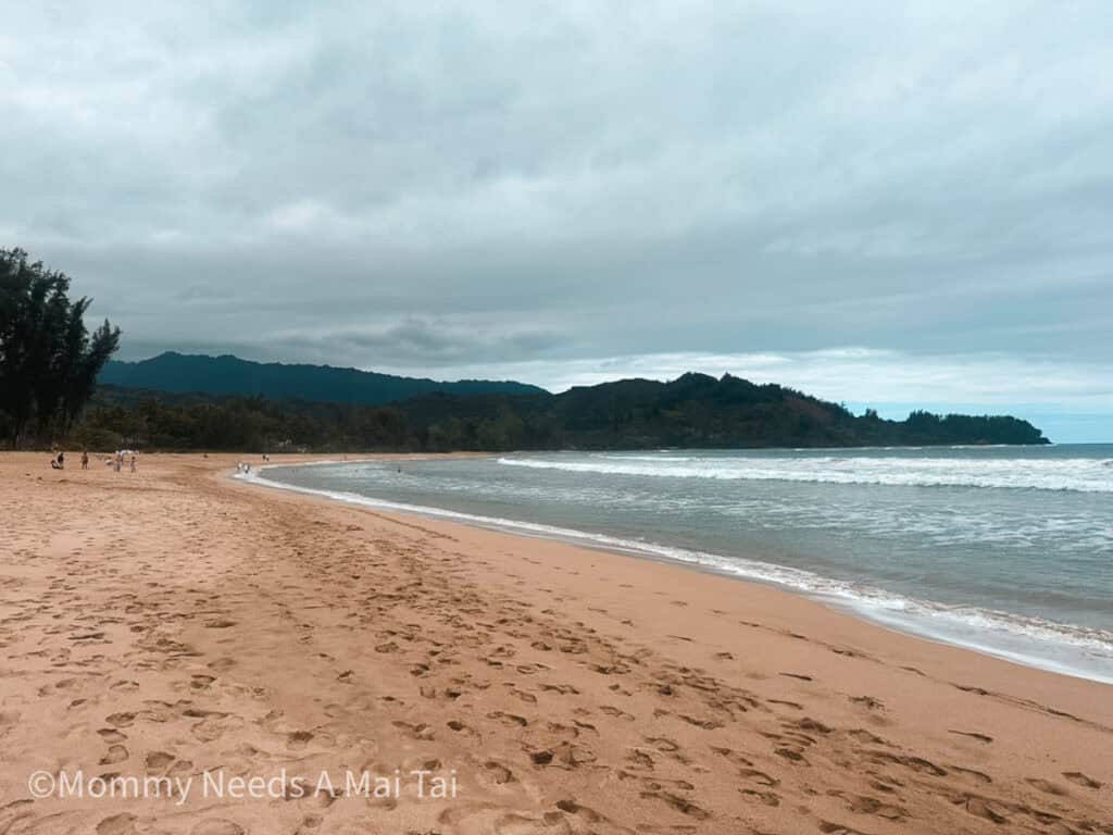 Hanalei Bay with blue water, mountains, and clouds in the distance. 